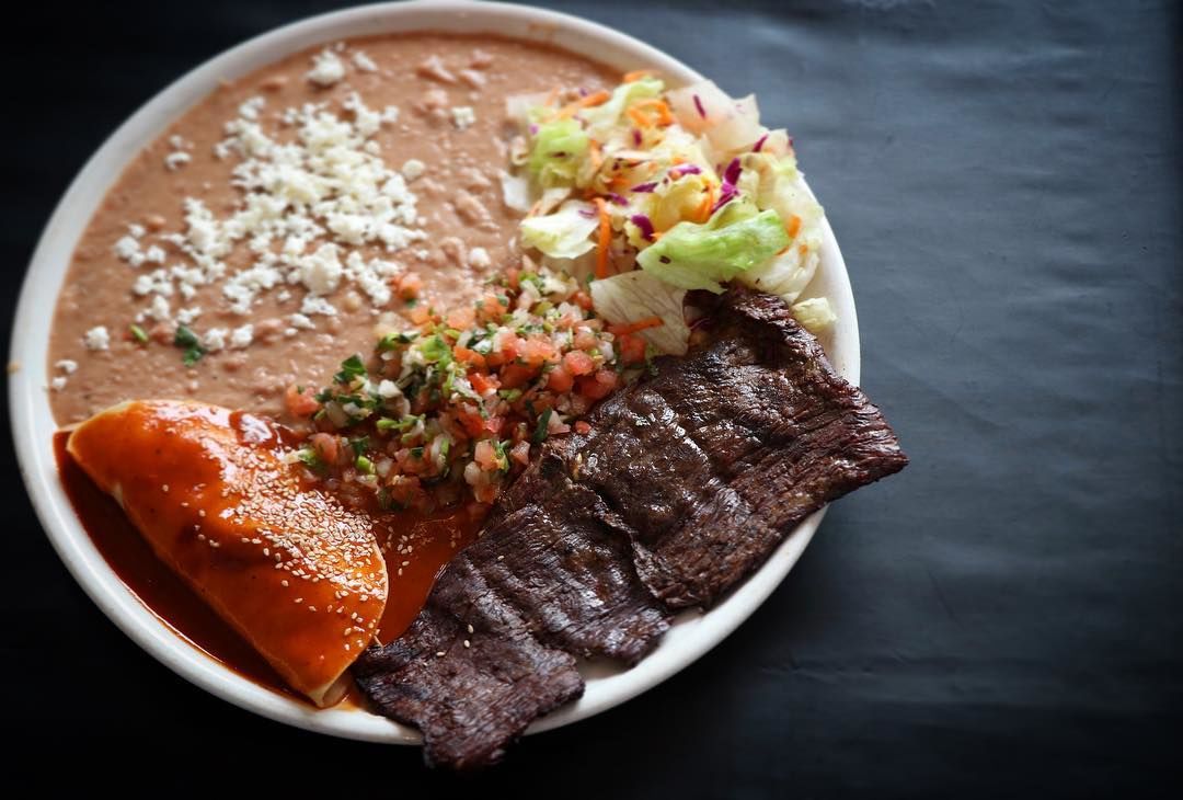 Steak a La Tampiquena: Grilled skirt steak garnished with a chicken “mole” sauce enchilada and refried beans, served with fresh salad.