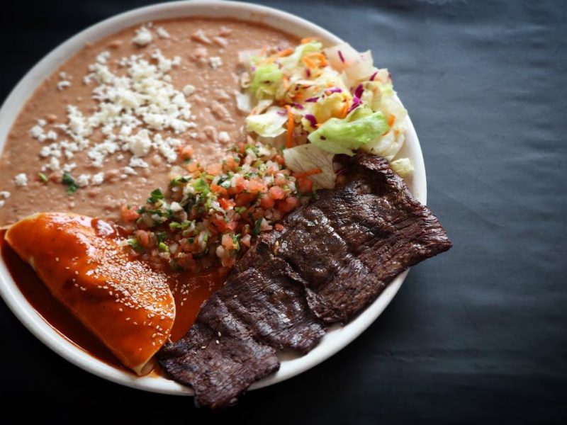 Steak a La Tampiquena: Grilled skirt steak garnished with a chicken “mole” sauce enchilada and refried beans, served with fresh salad.